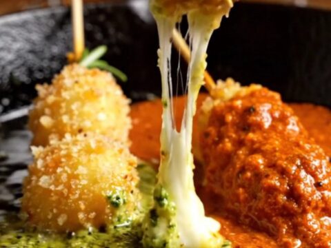 Golden-fried gnocchi skewers with a melted mozzarella core, served at a party.