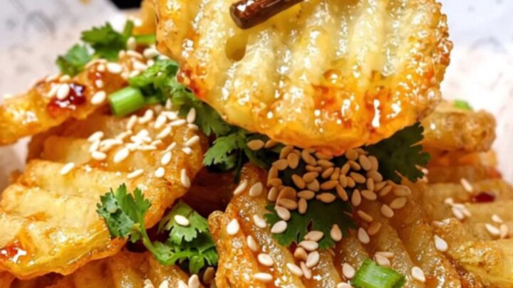 A close-up of crispy, golden-brown crinkle-cut potatoes glistening with chili oil and sprinkled with sesame seeds.