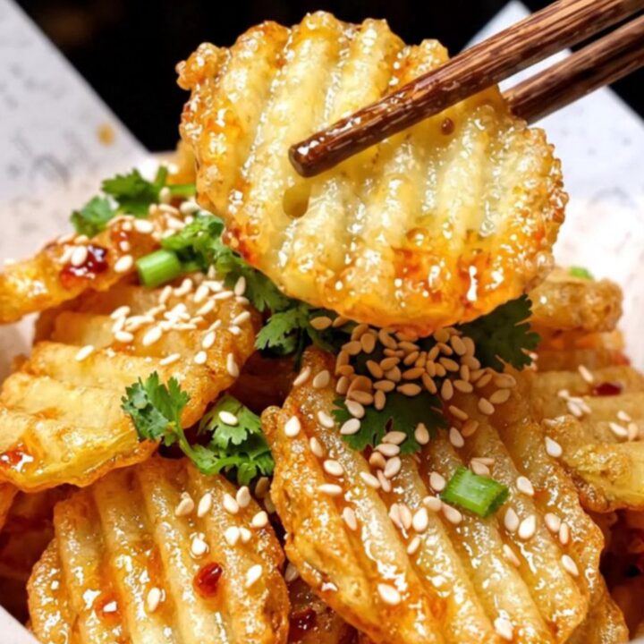 A close-up of crispy, golden-brown crinkle-cut potatoes glistening with chili oil and sprinkled with sesame seeds.