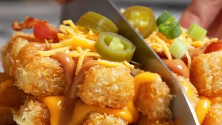 A golden, crispy smashed tater tot waffle lifted from a waffle iron, showing melted cheddar and jalapenos.