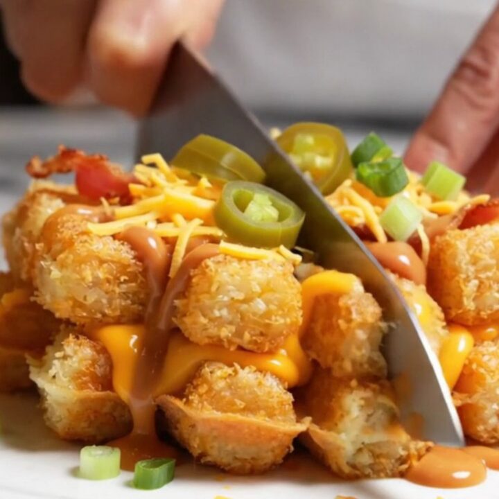 A golden, crispy smashed tater tot waffle lifted from a waffle iron, showing melted cheddar and jalapenos.