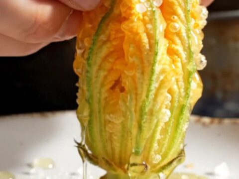 A close-up shot of a golden-fried zucchini blossom being pulled apart, revealing a creamy ricotta and mozzarella filling.