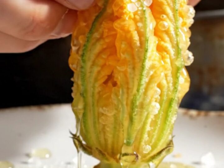 A close-up shot of a golden-fried zucchini blossom being pulled apart, revealing a creamy ricotta and mozzarella filling.