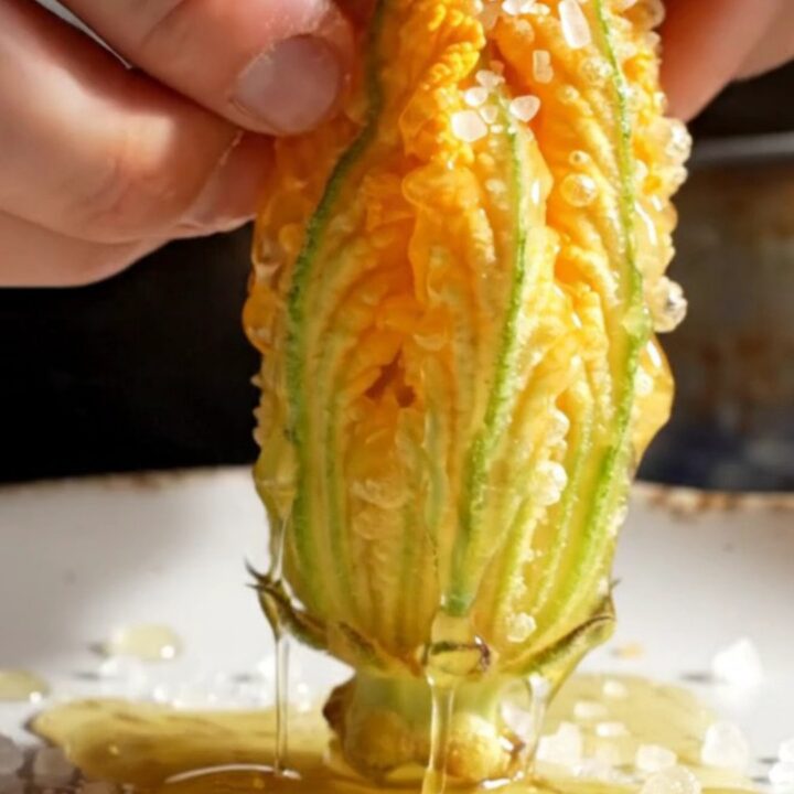 A close-up shot of a golden-fried zucchini blossom being pulled apart, revealing a creamy ricotta and mozzarella filling.