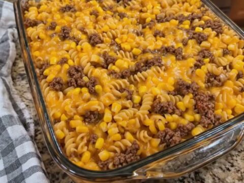 A close-up of a loaded cowboy cheeseburger casserole in a glass dish with a rich cheese pull.