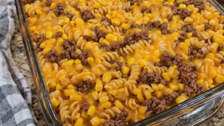 A close-up of a loaded cowboy cheeseburger casserole in a glass dish with a rich cheese pull.