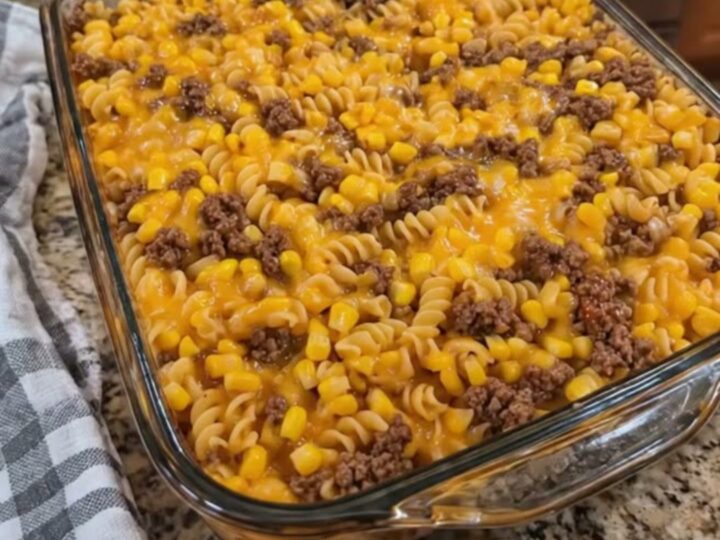 A close-up of a loaded cowboy cheeseburger casserole in a glass dish with a rich cheese pull.