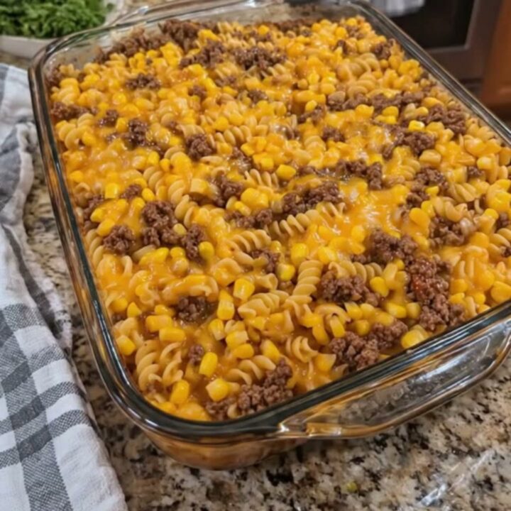 A close-up of a loaded cowboy cheeseburger casserole in a glass dish with a rich cheese pull.