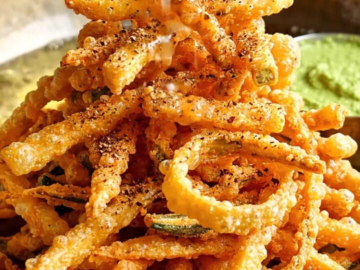 A golden, crispy plate of spiced okra fries served on a traditional brass platter with lime wedges.