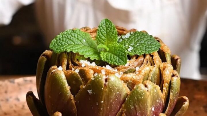 A golden, crispy Roman fried artichoke served on a rustic wooden table, with petals spread like a blooming flower.