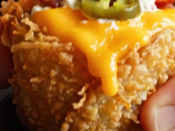 A close-up shot of a golden, crispy potato nest filled with molten cheese, bacon, and jalapeno, topped with cilantro.