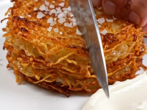 A golden-brown, woven potato stack in a skillet, displaying a crispy, detailed texture.