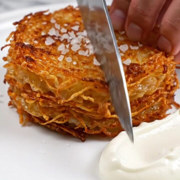 A golden-brown, woven potato stack in a skillet, displaying a crispy, detailed texture.