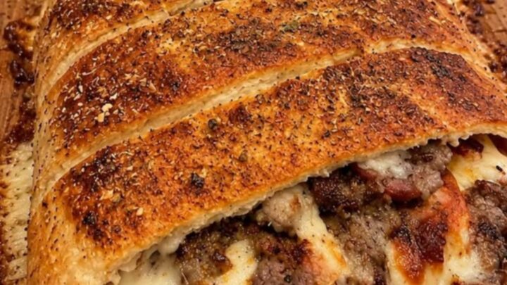 A golden-brown Philly cheesesteak stromboli sliced on a wooden board, with steam rising and visible melted cheese.