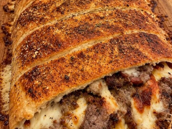 A golden-brown Philly cheesesteak stromboli sliced on a wooden board, with steam rising and visible melted cheese.
