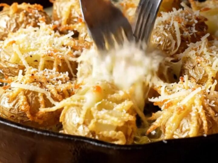 A cast-iron skillet filled with crispy smashed potatoes topped with melted Pecorino Romano and cracked black pepper.