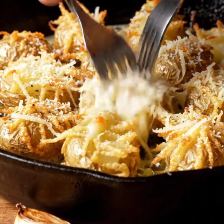 A cast-iron skillet filled with crispy smashed potatoes topped with melted Pecorino Romano and cracked black pepper.