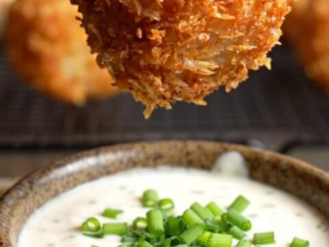 A close-up of a crispy bacon-wrapped tater tot bomb being pulled apart to reveal molten pepper jack cheese.