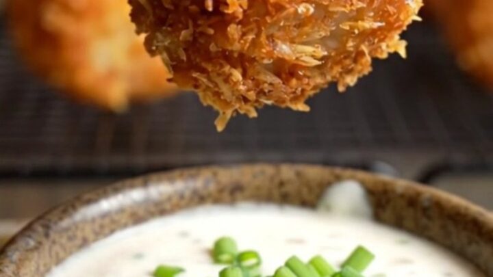 A close-up of a crispy bacon-wrapped tater tot bomb being pulled apart to reveal molten pepper jack cheese.