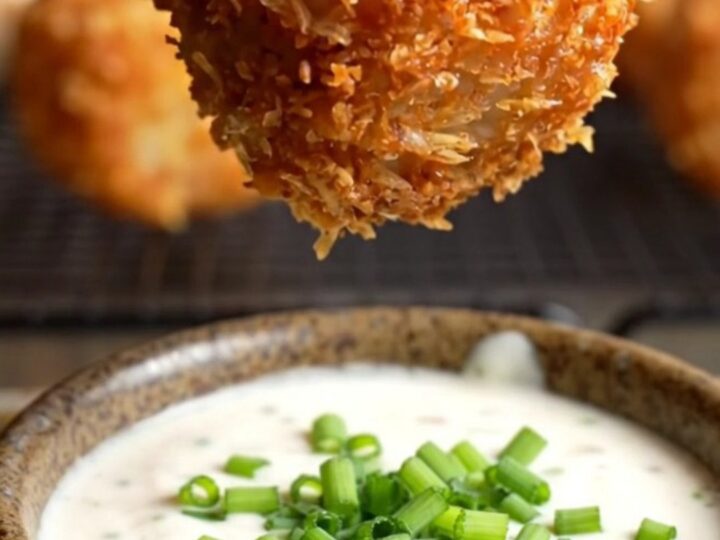 A close-up of a crispy bacon-wrapped tater tot bomb being pulled apart to reveal molten pepper jack cheese.