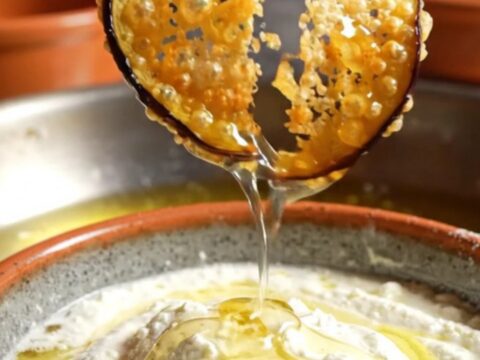A platter of golden-brown crispy eggplant chips drizzled with honey and served with a bowl of creamy whipped feta.