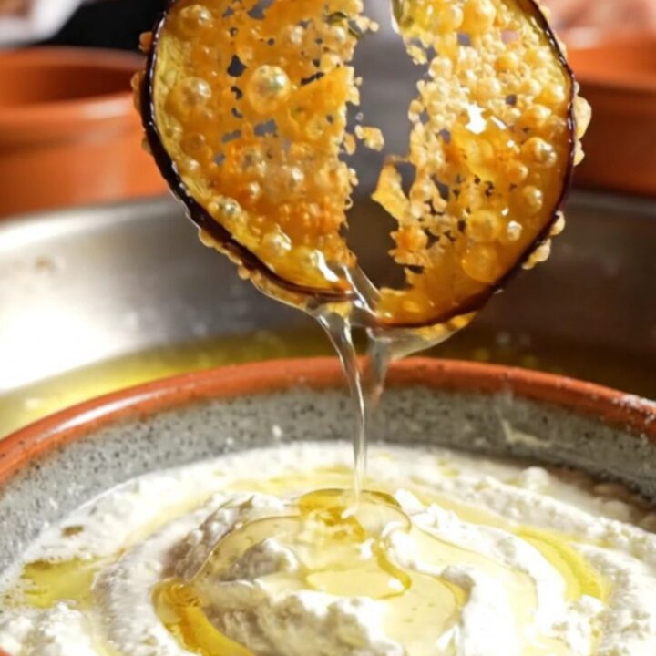 A platter of golden-brown crispy eggplant chips drizzled with honey and served with a bowl of creamy whipped feta.