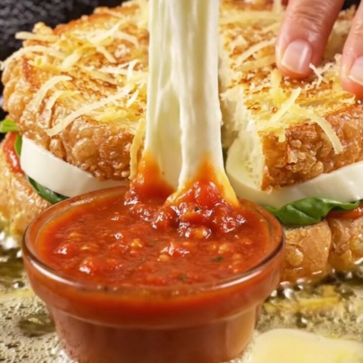 A golden-fried potato-crusted mozzarella sandwich being pulled apart with a long stretch of molten cheese.