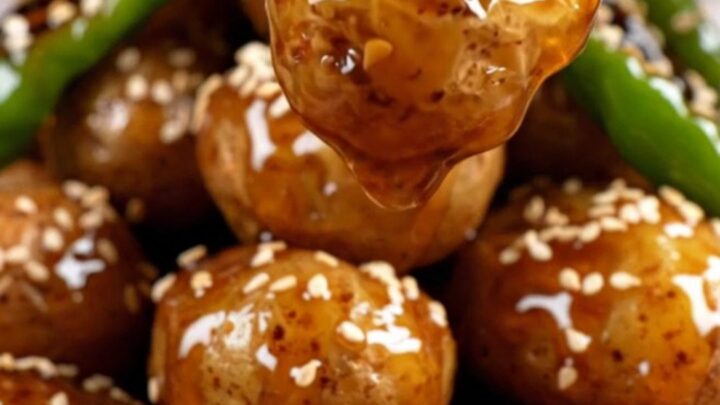 A close-up of crispy Korean baby potatoes glazed in a glossy soy-honey sauce with shishito peppers.