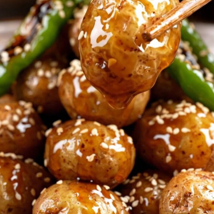 A close-up of crispy Korean baby potatoes glazed in a glossy soy-honey sauce with shishito peppers.