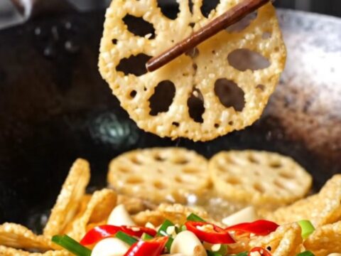 A towering pile of golden, crispy lotus root and potato slices garnished with red chilies and scallions.