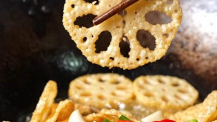 A towering pile of golden, crispy lotus root and potato slices garnished with red chilies and scallions.