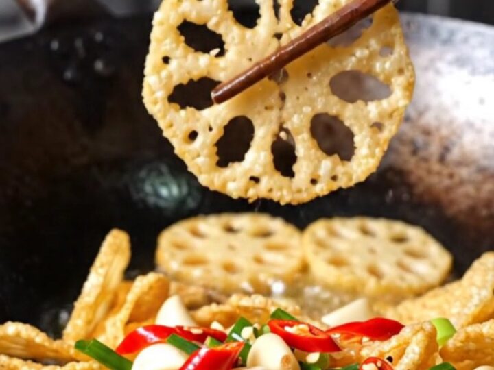 A towering pile of golden, crispy lotus root and potato slices garnished with red chilies and scallions.
