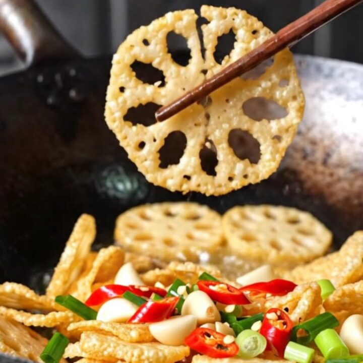 A towering pile of golden, crispy lotus root and potato slices garnished with red chilies and scallions.