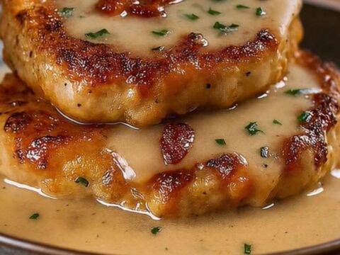 Golden-brown fried pork chops served in a ceramic dish and covered in a thick, creamy bacon gravy.