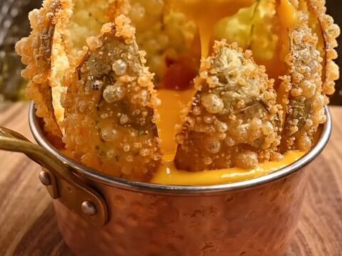 A golden, crispy blooming potato flower served with a side of warm beer cheese and bacon bits on a rustic wooden board.