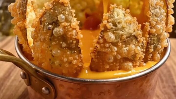 A golden, crispy blooming potato flower served with a side of warm beer cheese and bacon bits on a rustic wooden board.