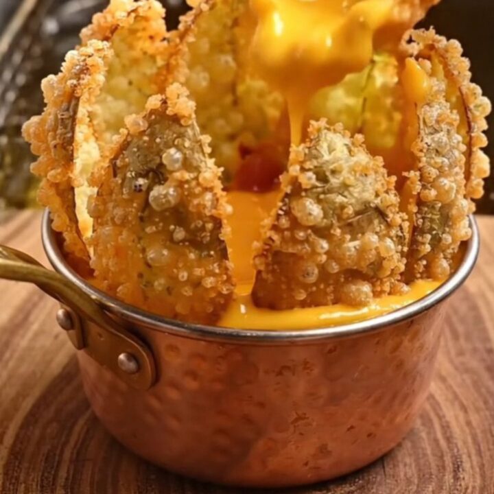 A golden, crispy blooming potato flower served with a side of warm beer cheese and bacon bits on a rustic wooden board.