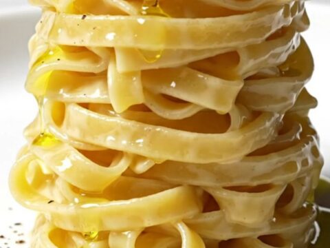 A close-up of perfectly cooked tonnarelli pasta coated in a creamy, pepper-speckled Pecorino Romano sauce.