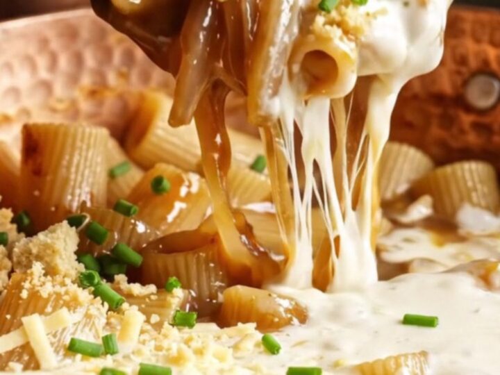 A close-up of rigatoni pasta coated in a dark, rich onion sauce with strings of melted Gruyère cheese.