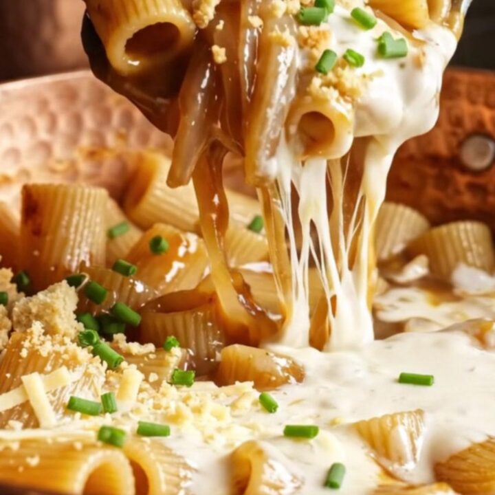 A close-up of rigatoni pasta coated in a dark, rich onion sauce with strings of melted Gruyère cheese.