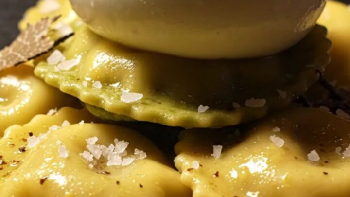 A close-up of ricotta ravioli covered in a glossy brown butter sauce with shaved black truffles.
