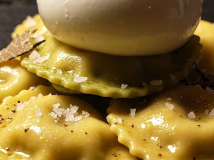 A close-up of ricotta ravioli covered in a glossy brown butter sauce with shaved black truffles.