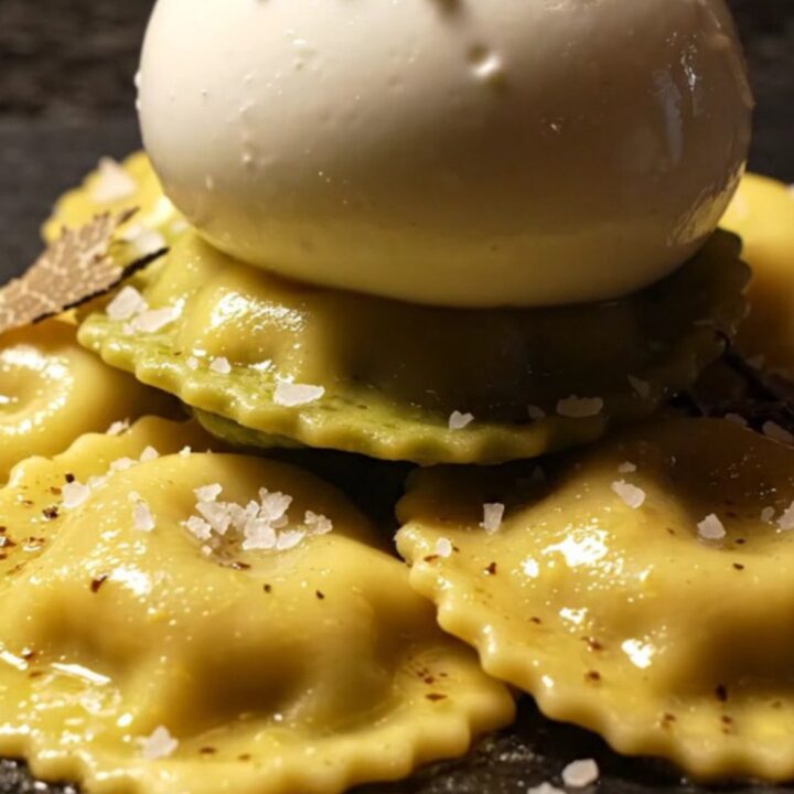 A close-up of ricotta ravioli covered in a glossy brown butter sauce with shaved black truffles.