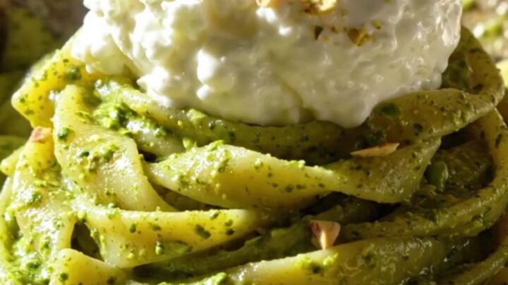 A close-up of twisted trofie pasta coated in bright green pistachio pesto and topped with creamy stracciatella.