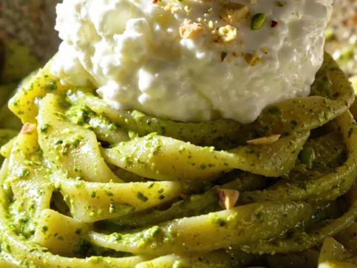 A close-up of twisted trofie pasta coated in bright green pistachio pesto and topped with creamy stracciatella.