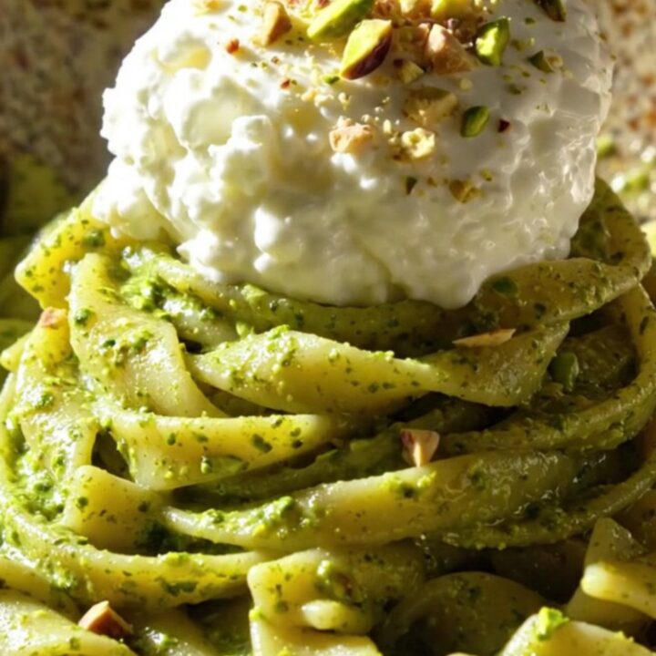 A close-up of twisted trofie pasta coated in bright green pistachio pesto and topped with creamy stracciatella.