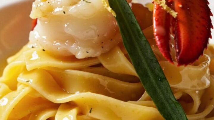 A close-up of butter-poached lobster medallions resting on ruffled mafaldine pasta with a golden saffron butter sauce.