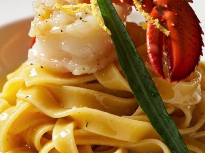 A close-up of butter-poached lobster medallions resting on ruffled mafaldine pasta with a golden saffron butter sauce.