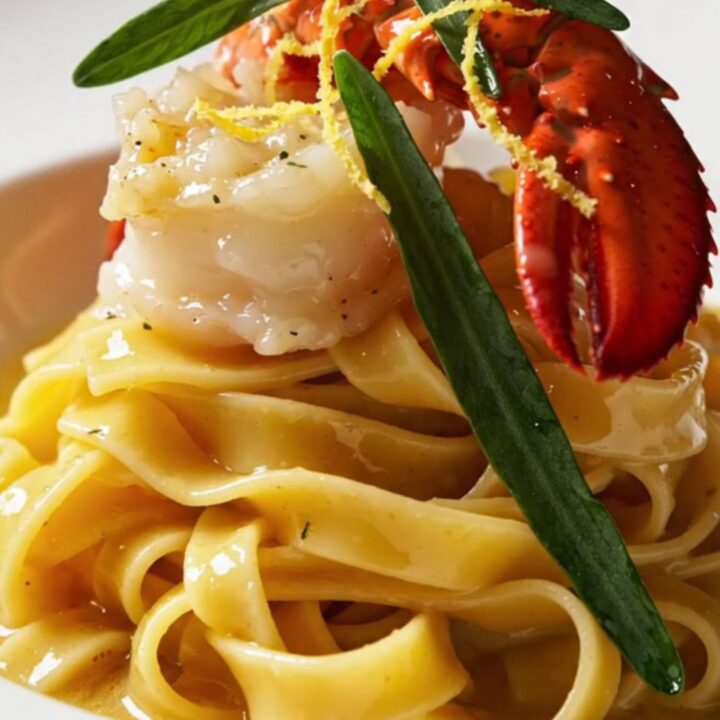 A close-up of butter-poached lobster medallions resting on ruffled mafaldine pasta with a golden saffron butter sauce.