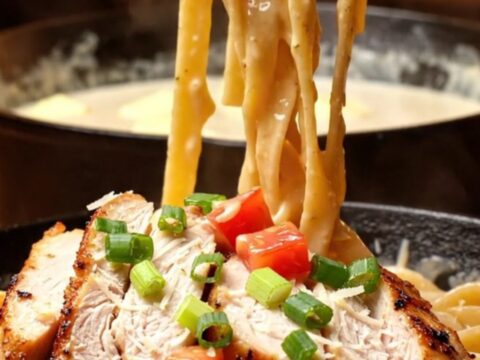 A plate of fettuccine pasta tossed in creamy Cajun Alfredo sauce topped with blackened chicken slices.